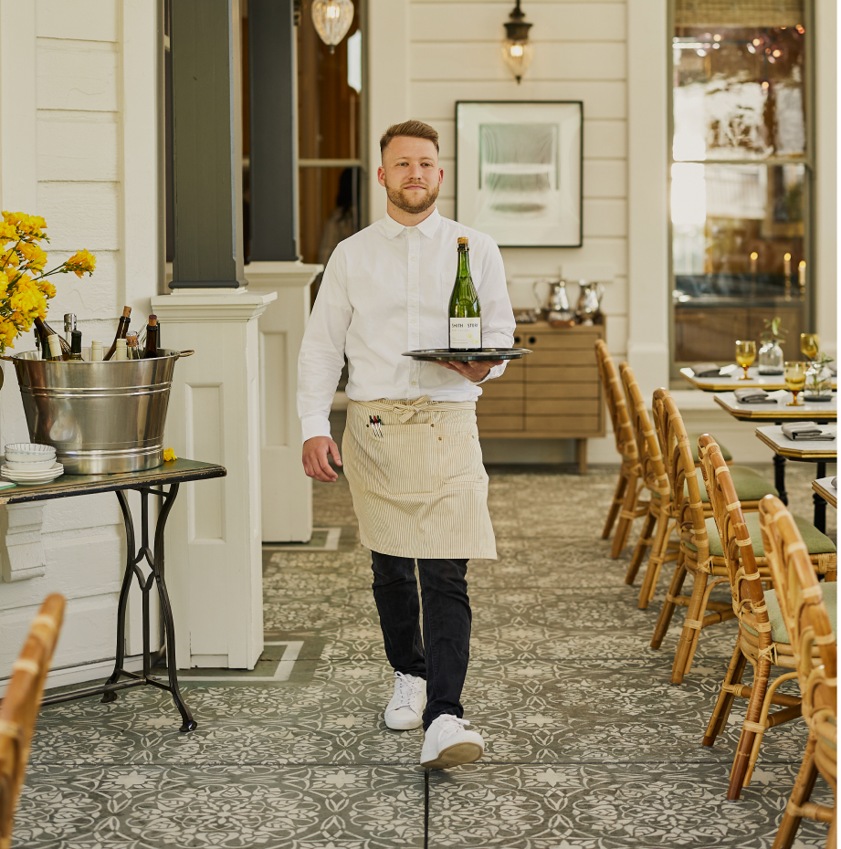 Server carrying a bottle of wine on a silver tray in an elegant restaurant